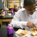 A smiling student sitting in a classroom, eating an orange during snack time. thumbnail