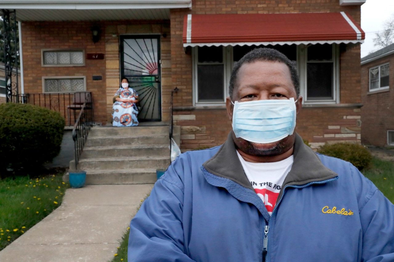 Anthony Travis, who has recovered from COVID-19 and lives with his sister, Jacqueline K. Johnson, background, and an adult daughter, poses for a portrait outside his Riverdale, Ill., home on Thursday, April 23, 2020. Travis, who's diabetic, has high blood pressure and is a cancer survivor, must self isolate within the home as a matter of taking care of one another. (AP Photo/Charles Rex Arbogast)