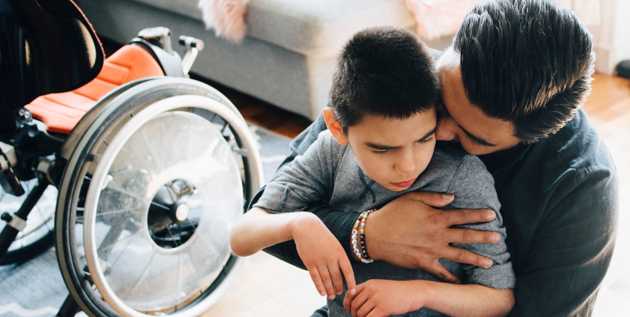 A father sitting on a floor,  holding his son.