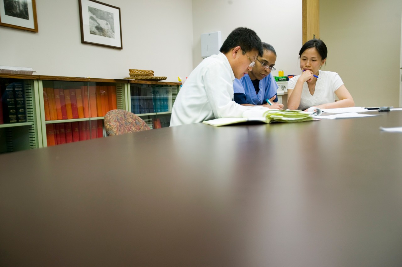 Doctor showing pill bottle to patient at home - wearing face mask