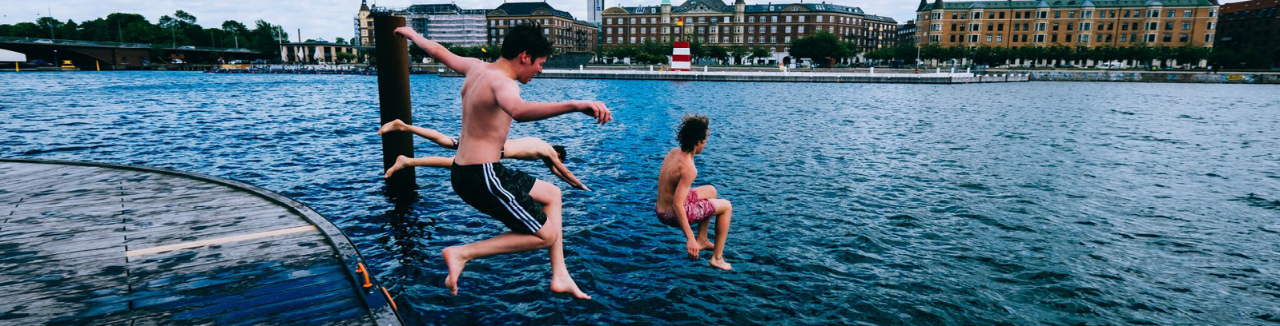 Boys jumping in a river in swim trunks.