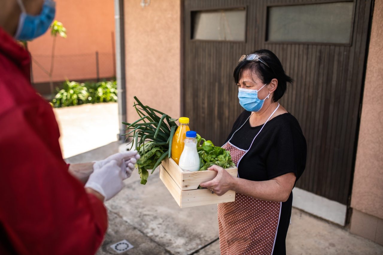 Woman wearing protective mask taking groceries from a volunteer.