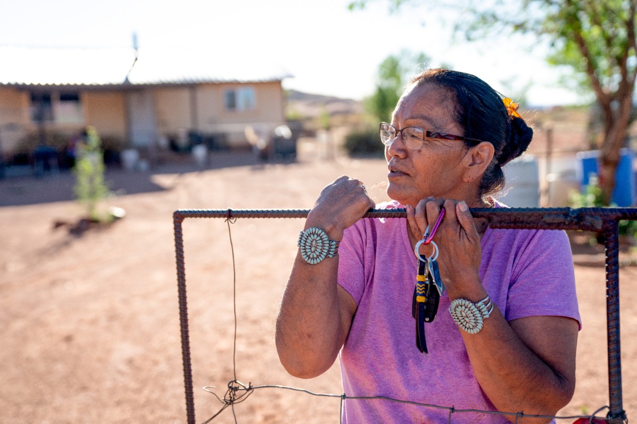 A Navajo woman standing by the gate of her home, with a faraway look in her eyes wondering if life will ever be back to normal, Covid19