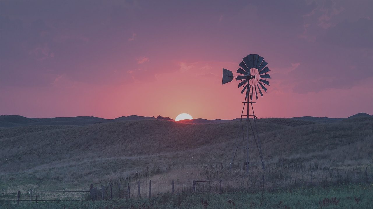 A windmill-driven water pump standing on the horizon during sunsets.