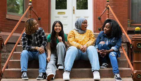 A multicultural group of girls sitting on the steps outside a townhouse.