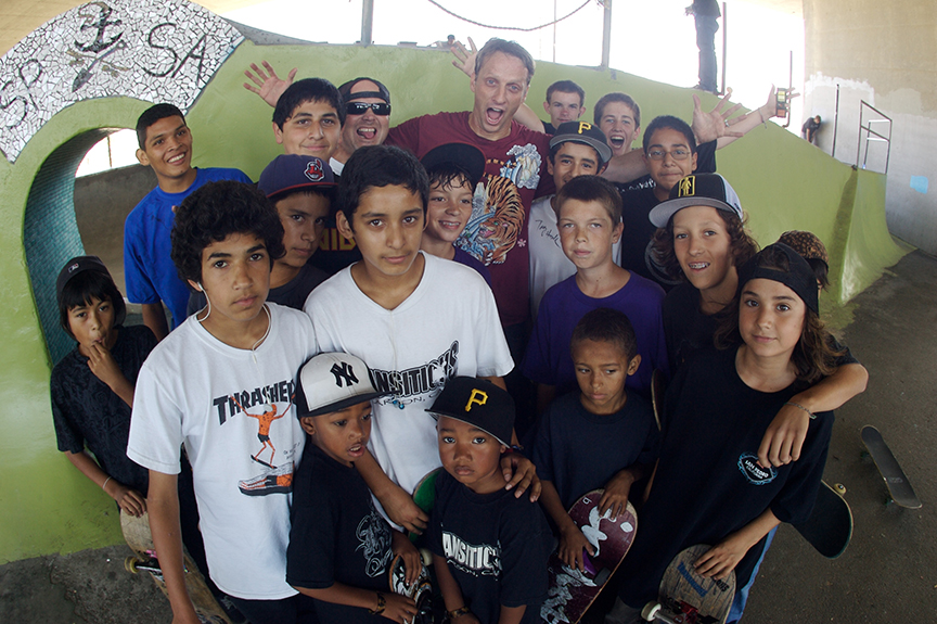 Photo of kids ages 6 to 16 holding skateboards and standing with Tony Hawk at one of his Foundation's skateparks.