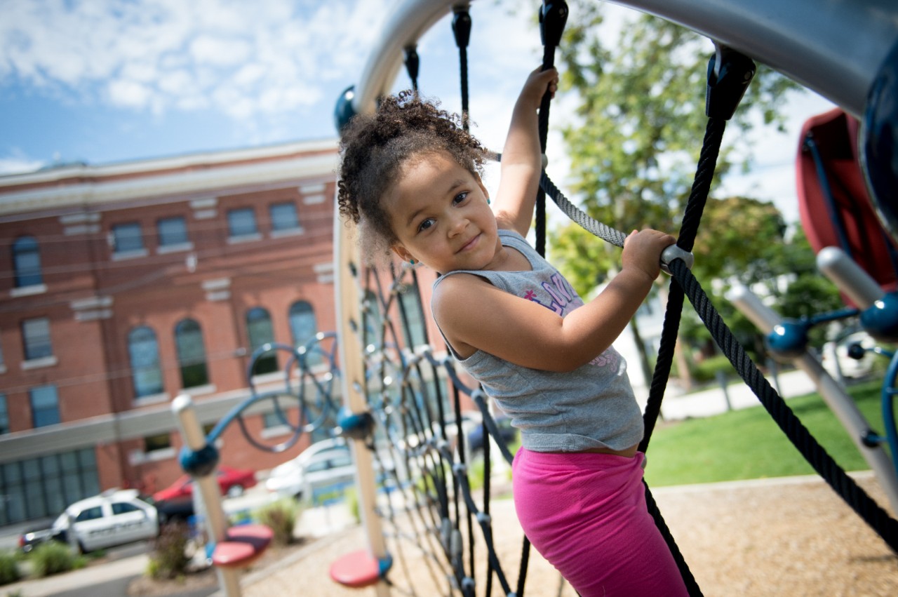 A young girl playing on a playground jungle gym.