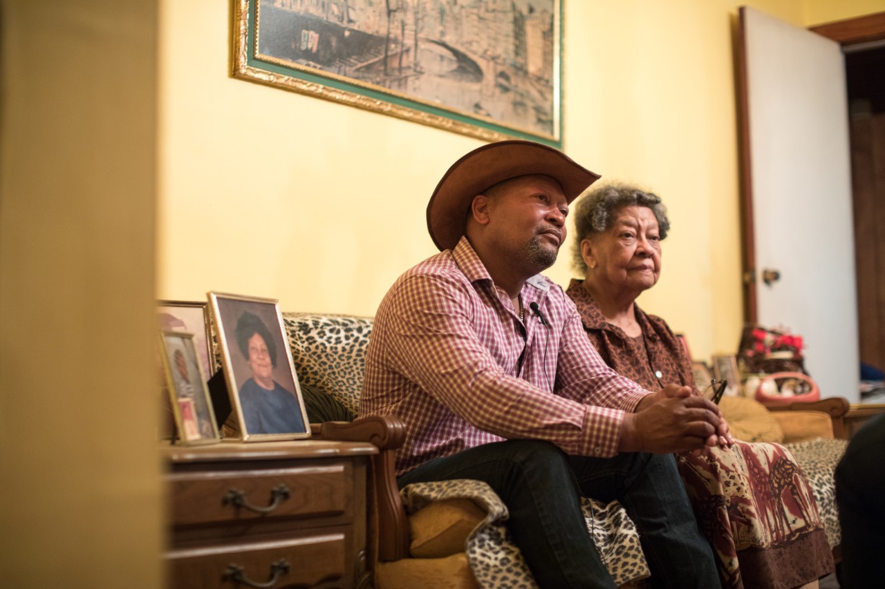 A man sits with his mother in her living room. Alabama 2019 - Black Belt. Land belonging to Ja'mestican Parham. His great Grandfather bought this land somewhere between 1868 and 1870 (from the Hope family). Originallly $600 was paid for 700 acres. This amount is now down to 200 acres and Ja'mestican beleives it has been taken away immorally over the years by several forces and people. It is now designated as Forest Land and Ja'mestican has planted much of it by hand. His mother Ethel Parham is seen on the right.
