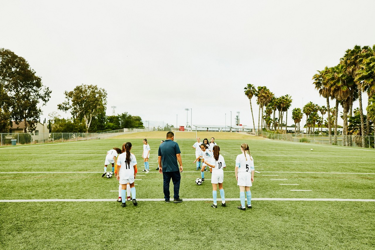 Soccer coach watching young female players run drills during practice