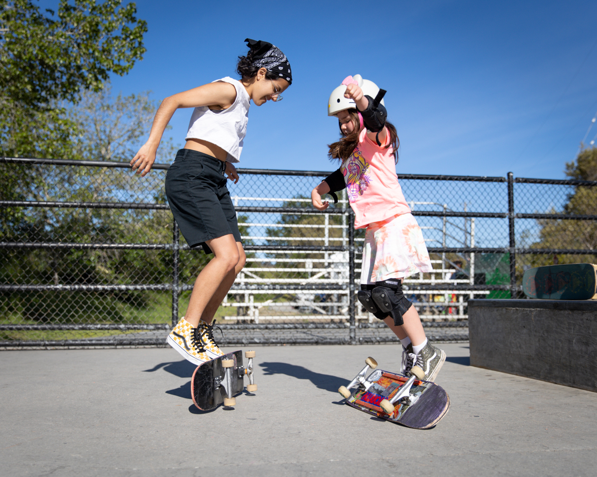 Two girls flip skateboards over with their feet.