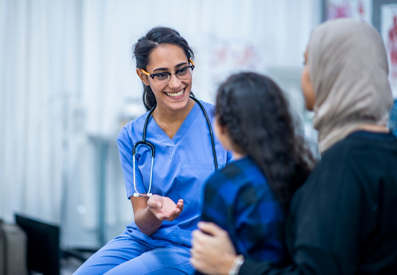 An Ethnic mother and daughter are indoors in a hospital. The daughter is about to have a checkup. Her mother and doctor are trying to comfort her.