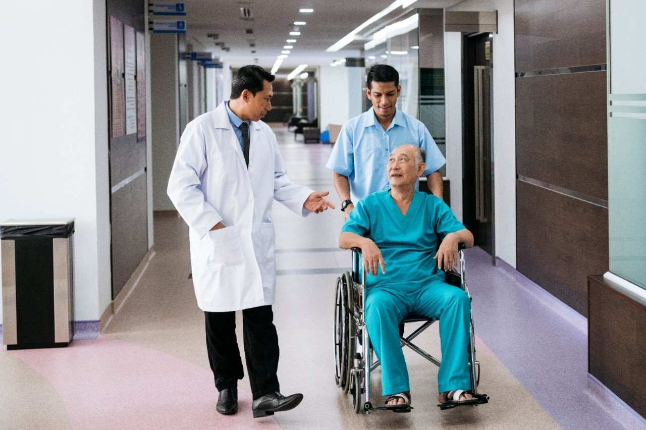 A porter pushing a patient in a wheelchair along a corridor.