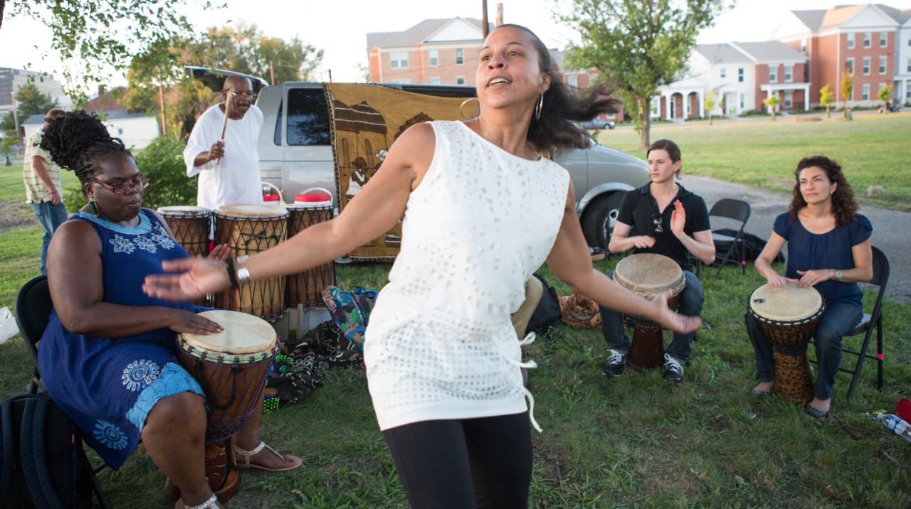 A woman dancing to the beat of a drum group in a park.