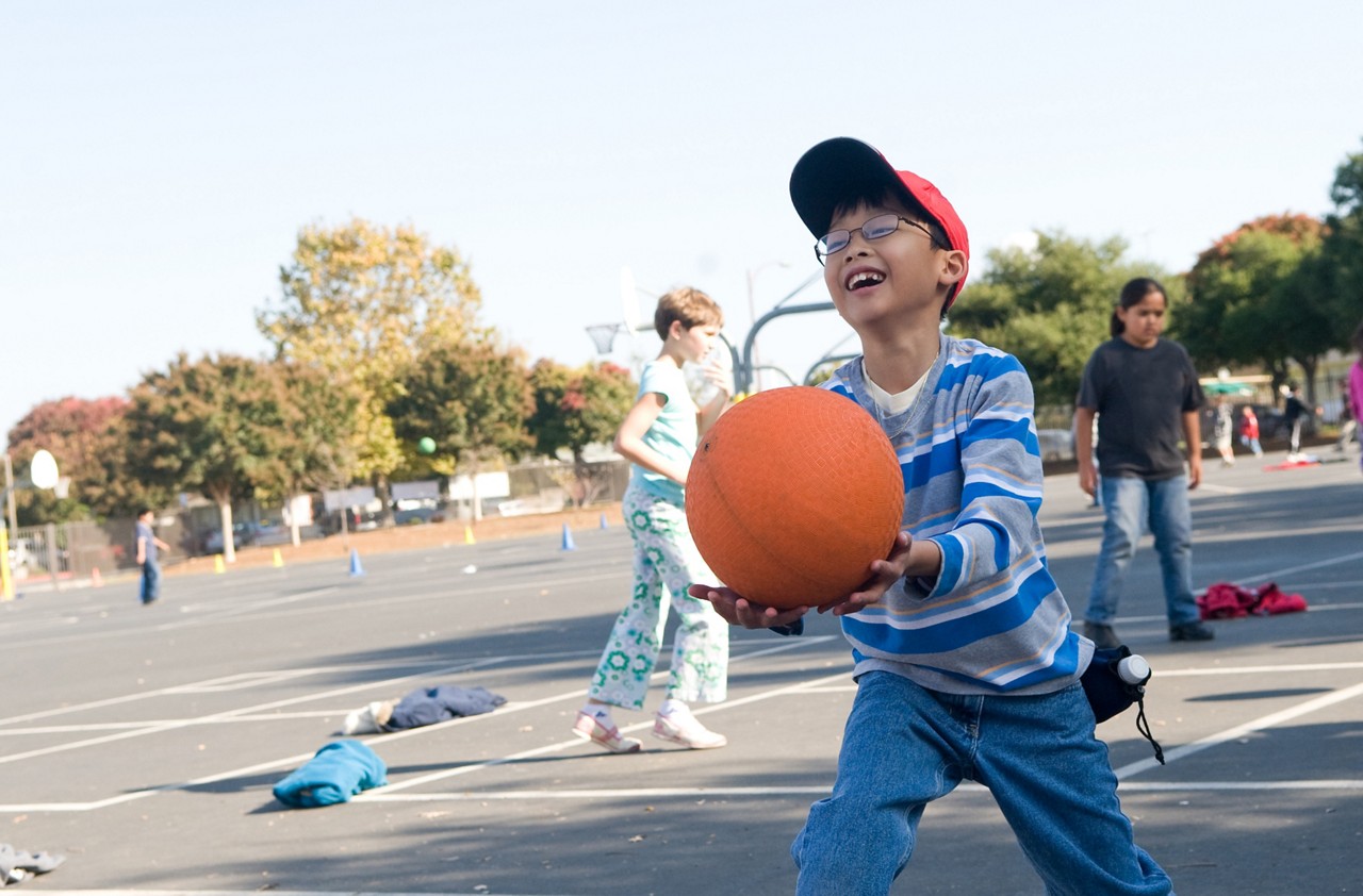 Young boy having fun with a basket ball at an outdoor playground. Horizontal flip.