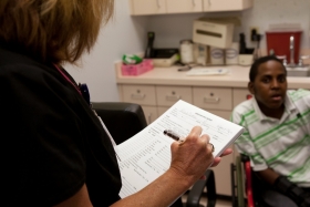A patient sits in a doctor's office while a nurse looks over his chart. 