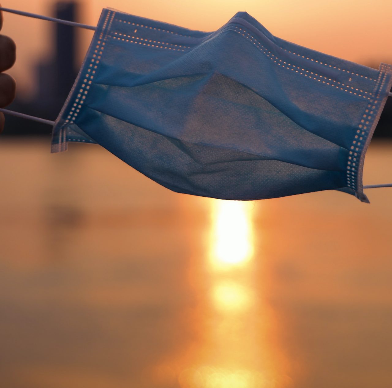Two hands holding opposite ends of a mask in front of a sunset.