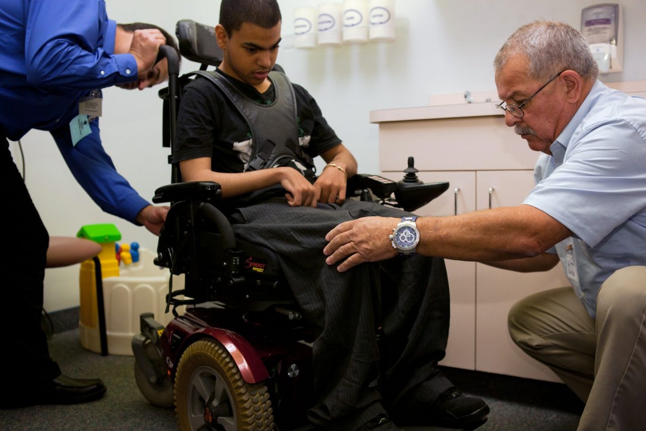 Health professionals fit a disabled teenage boy in a wheelchair.