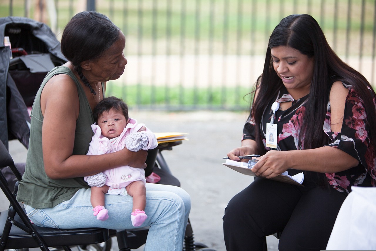 A medical professional talking with a woman holding an infant. A medical professional talking with a woman holding an infant.