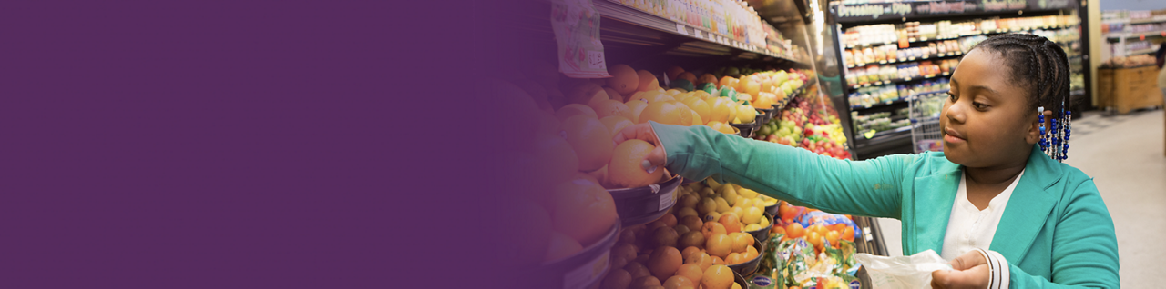A girl chooses an orange from a bin at a food store.