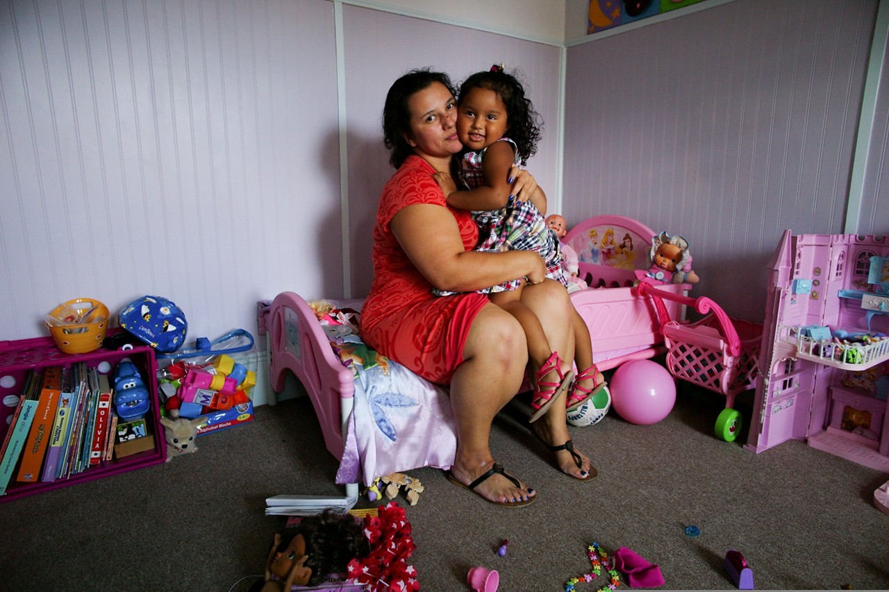 A mother and daughter sit together amidst toys and books. A mother and daughter sit together amidst toys and books.
