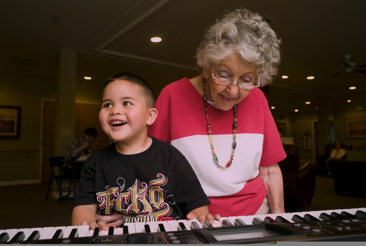 A nursing home resident teaches a young boy to play the organ. A nursing home resident teaches a young boy to play the organ.