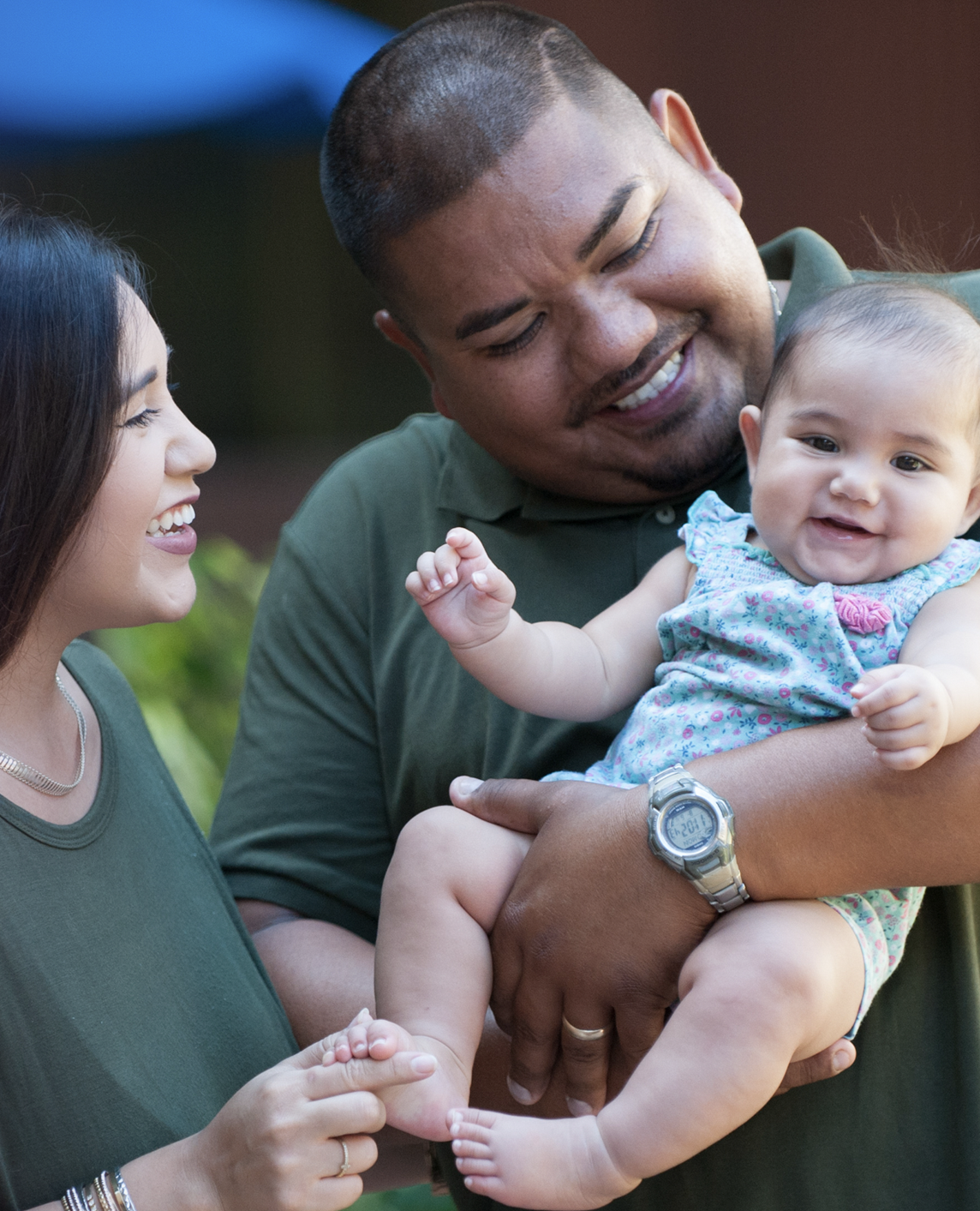 A mother and father smile at their toddler while she eats watermelon. A mother and father smile at their toddler while she eats watermelon.
