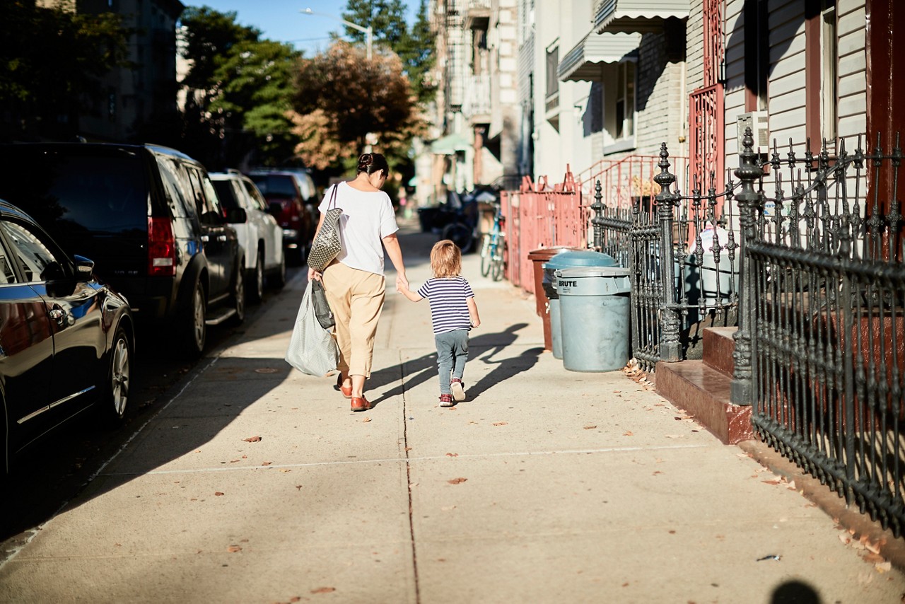A mother holds her young daughter's hand while walking on a city sidewalk. A mother holds her young daughter's hand while walking on a city sidewalk.