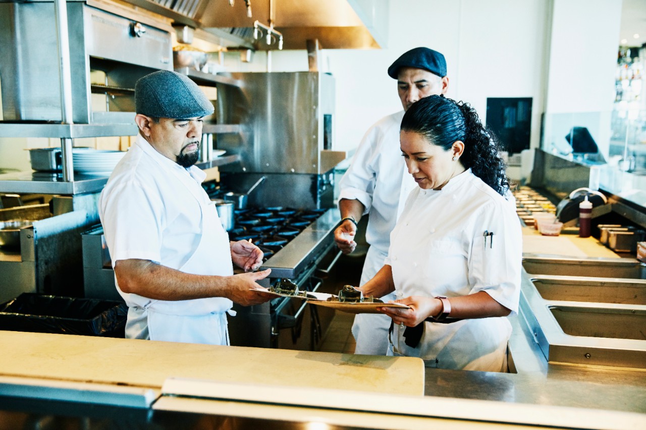 Female chef reviewing orders with kitchen staff in restaurant kitchen