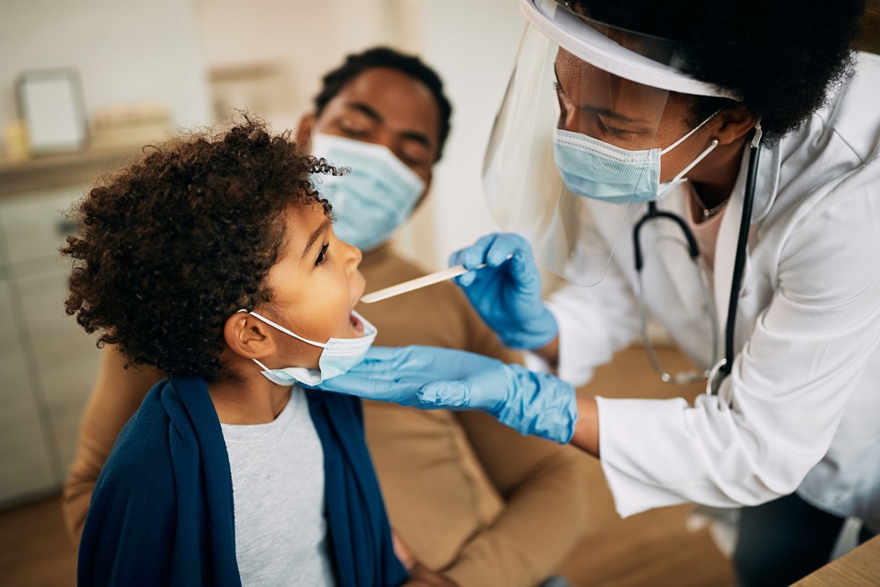 Family doctor examining throat of a small black boy while visiting him at home during coronavirus pandemic. Family doctor examining throat of a small black boy while visiting him at home during coronavirus pandemic.