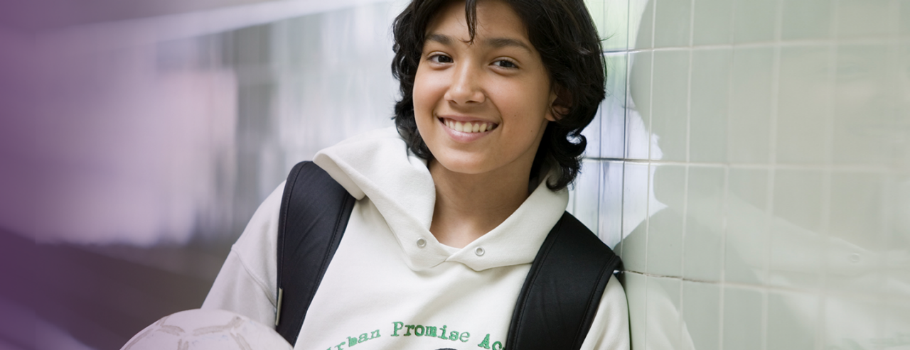 A high school student holding a soccer ball in a school hallway.