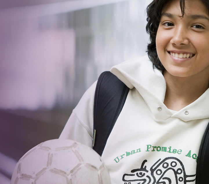 A high school student holding a soccer ball in a school hallway.