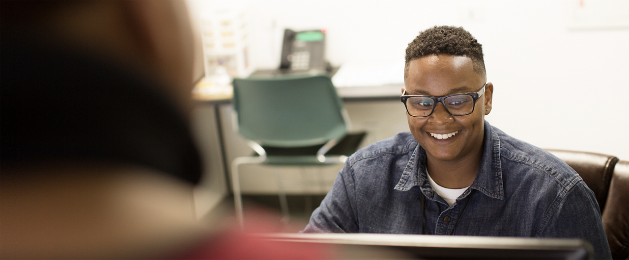 A smiling man looks at a computer monitor.