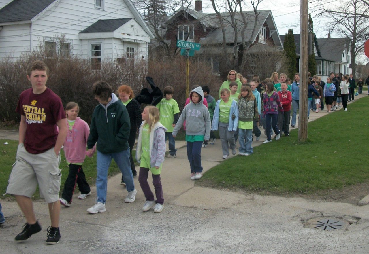 Students and teachers walking to school using a sidewalk.