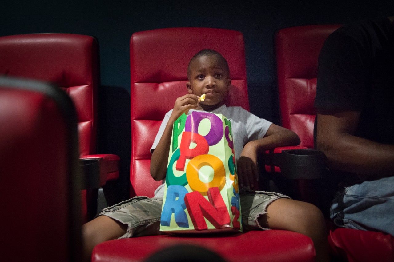 A young moviegoer enjoys popcorn at the 24:1 Cinema on Page Ave., one of the new constructions in Pagedale which was constructed with the assistance of Beyond Housing to revitalize commerce downtown. The cinema offers tickets at lower prices than many other movie theaters, and a portion of the proceeds returns to the 24:1 communities to fund new initiatives.