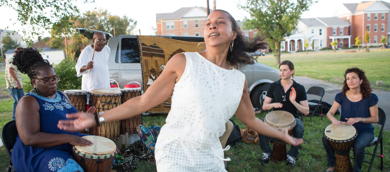 A woman dancing to the beat of a drum group in a park.