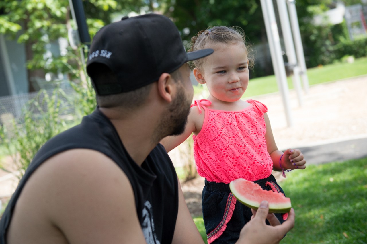 A father and his daughter enjoying fresh watermelon while at a park.