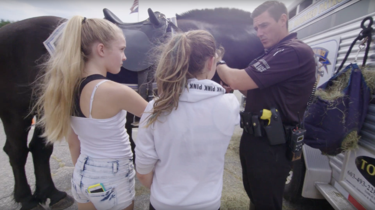 Two teen girls speaking with a police officer standing next to his horse.