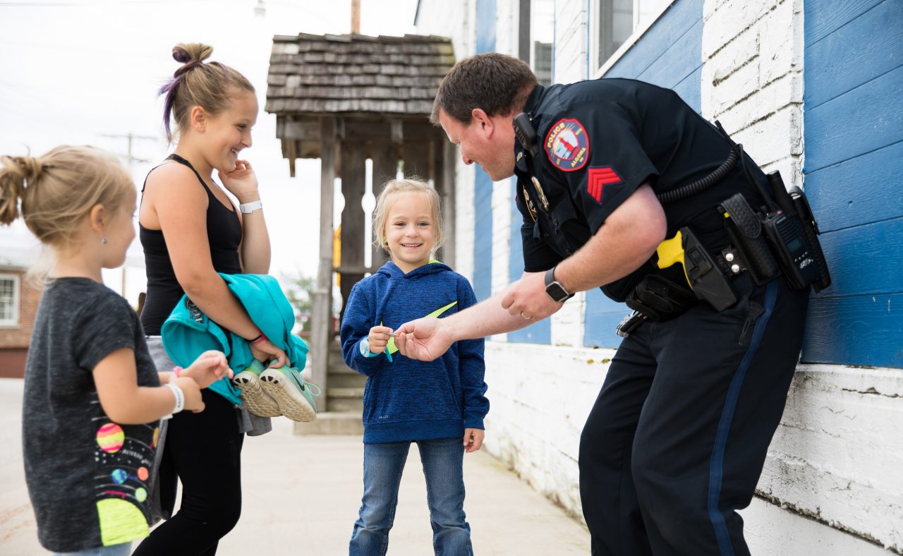 A policeman hands out stickers to three girls. 