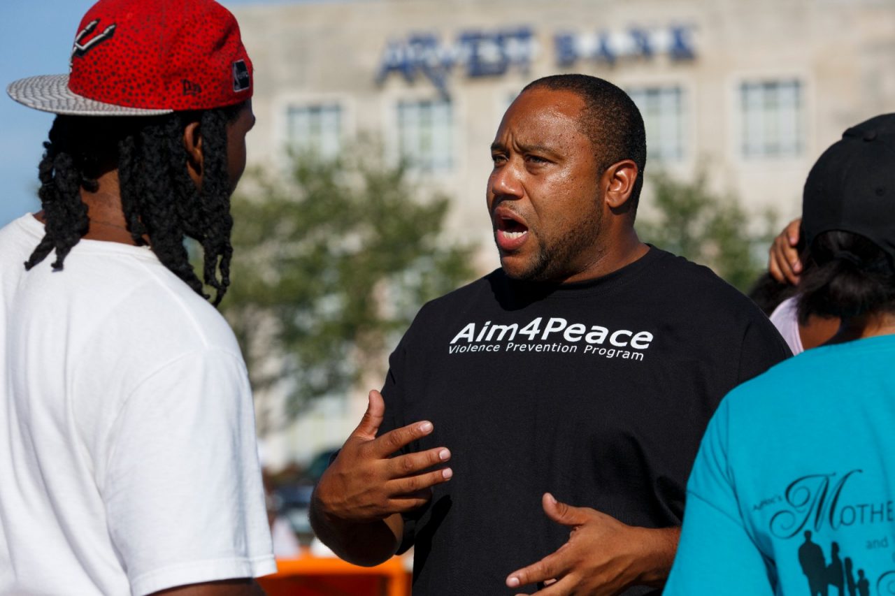 Rashid Junaid talks with a community member at an Aim4Peace barbecue in Kansas City, MO. Junaid is a violence prevention manager with Aim4Peace, which takes a public health approach to violence, treating it like a disease that spreads and must be contained. The intervention teams go into the community and the hospitals to work directly with at-risk individuals, friends and families.