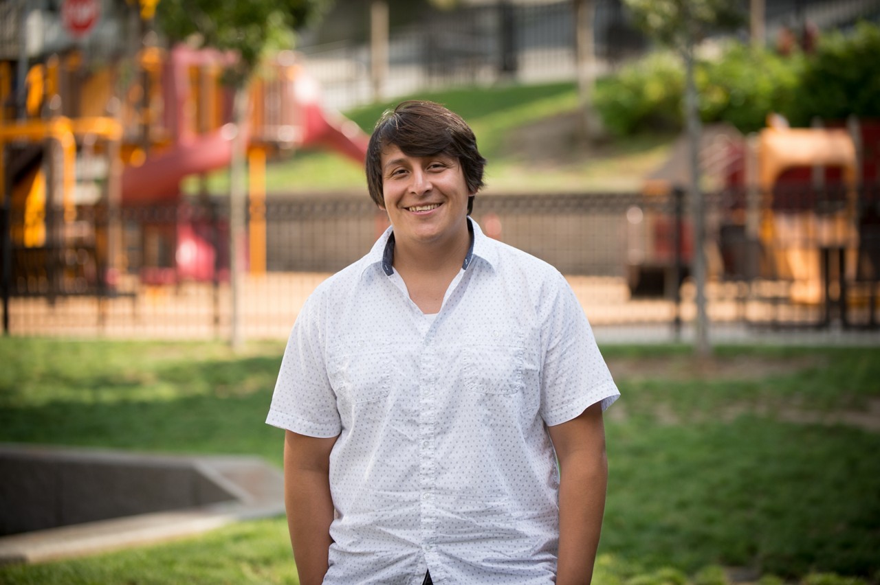 A man in a white shirt stands in front of a playground.