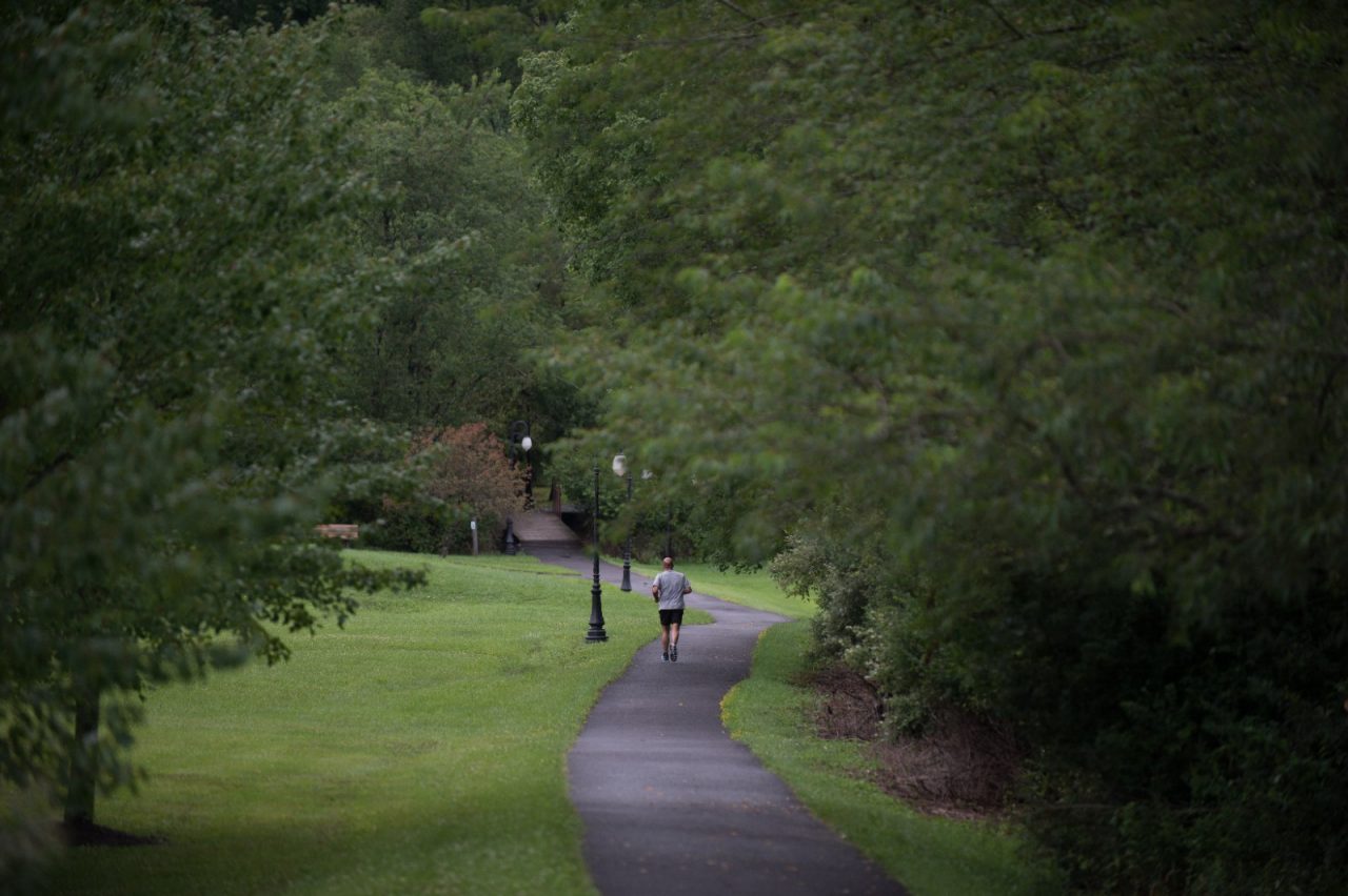A man runs on a trail through with overgrown trees on either side.