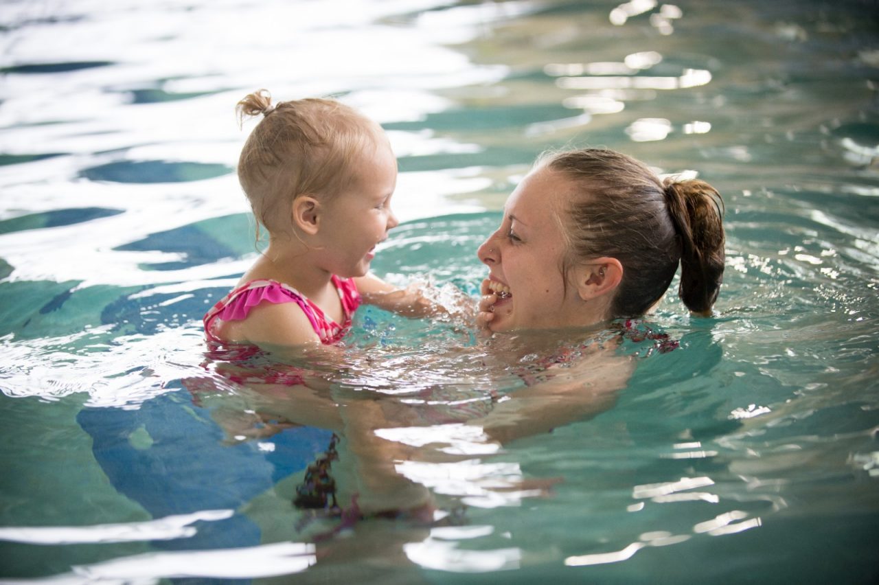 A mother holding her toddler daughter in a community pool. 