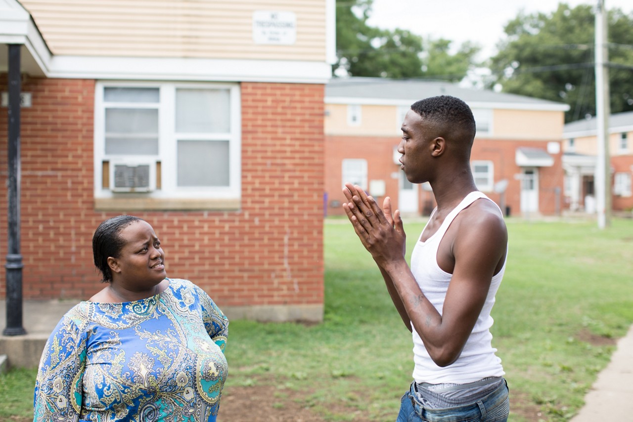 Two people talking in the front yard of an apartment complex.. 