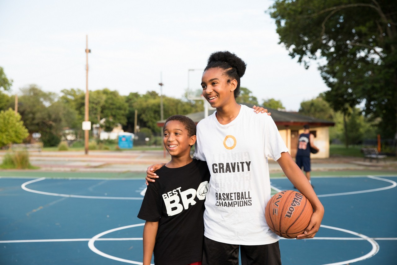 Happy siblings holding a basketball on the court.