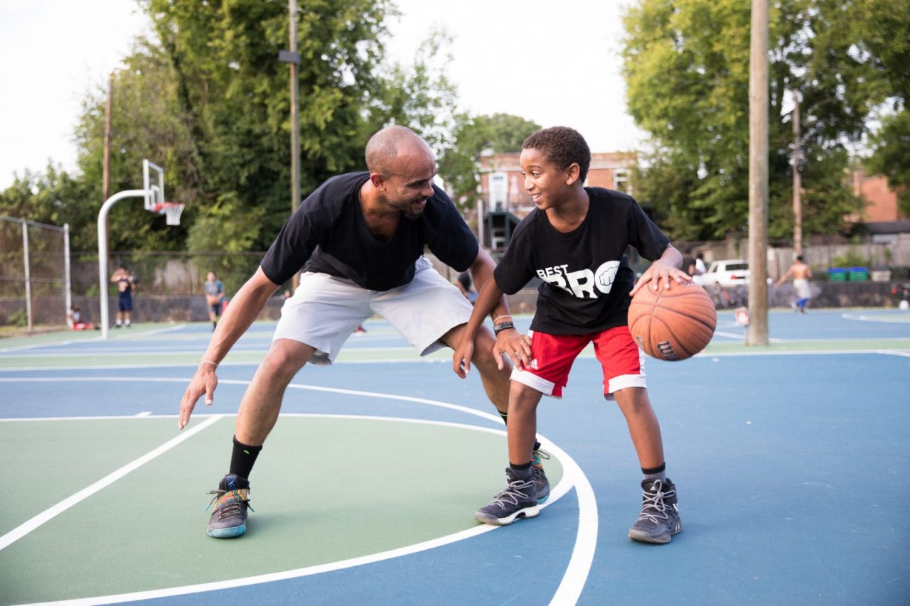 A father and son playing basketball together. 