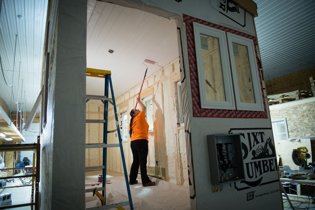 A woman painting the ceiling of a partially constructed house.