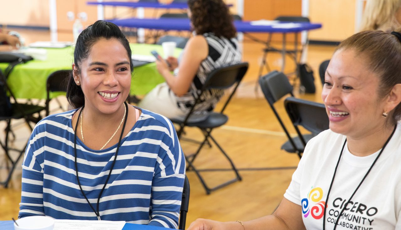 Two women smiling and sitting together at a community event.