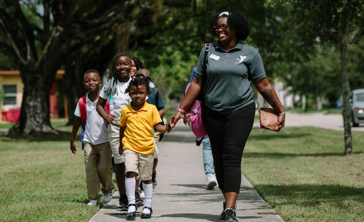 A woman and a class of young children walking on a sidewalk.