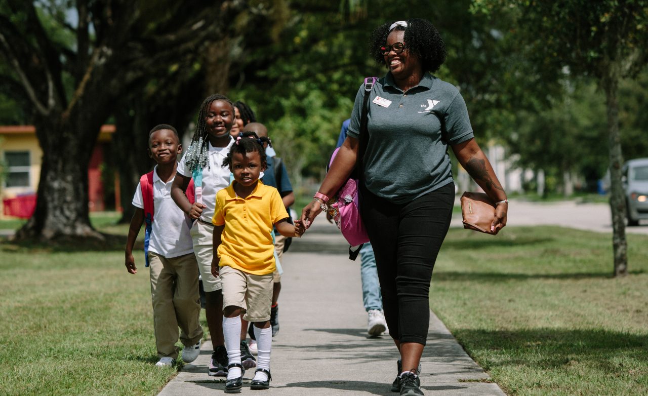 A woman and a class of young children walking on a sidewalk.