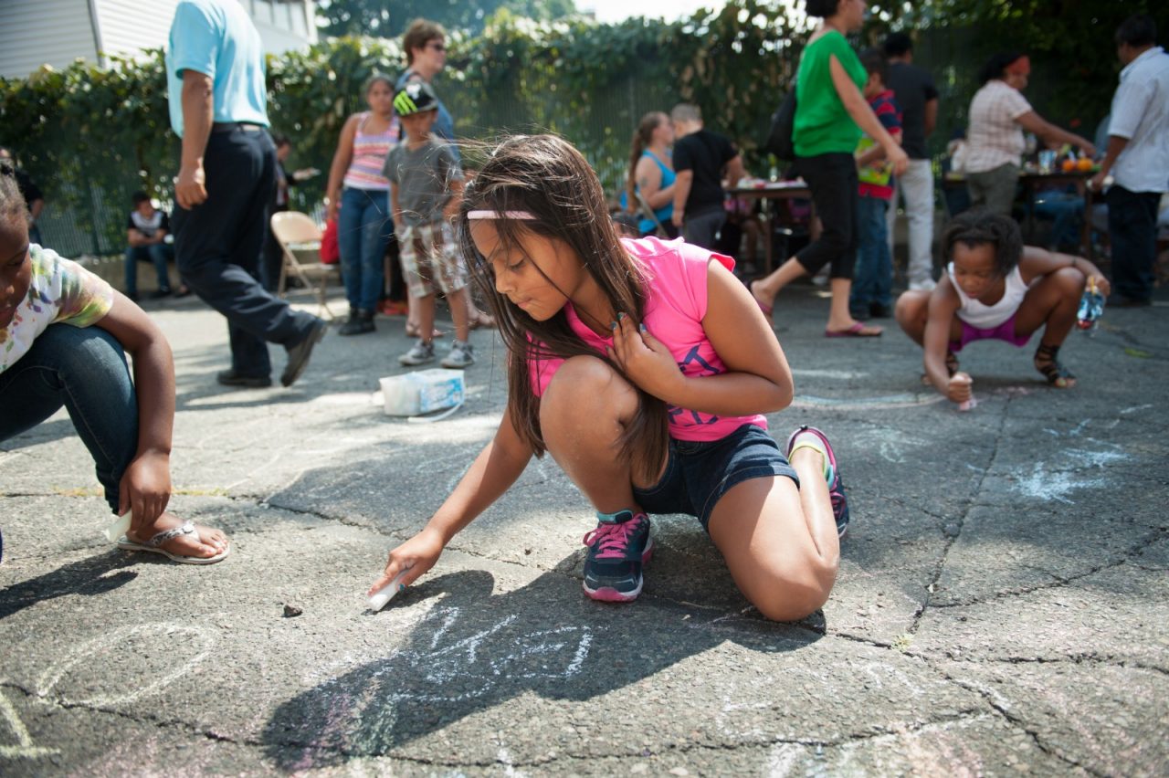 A young girl enjoys drawing on the pavement with chalk.